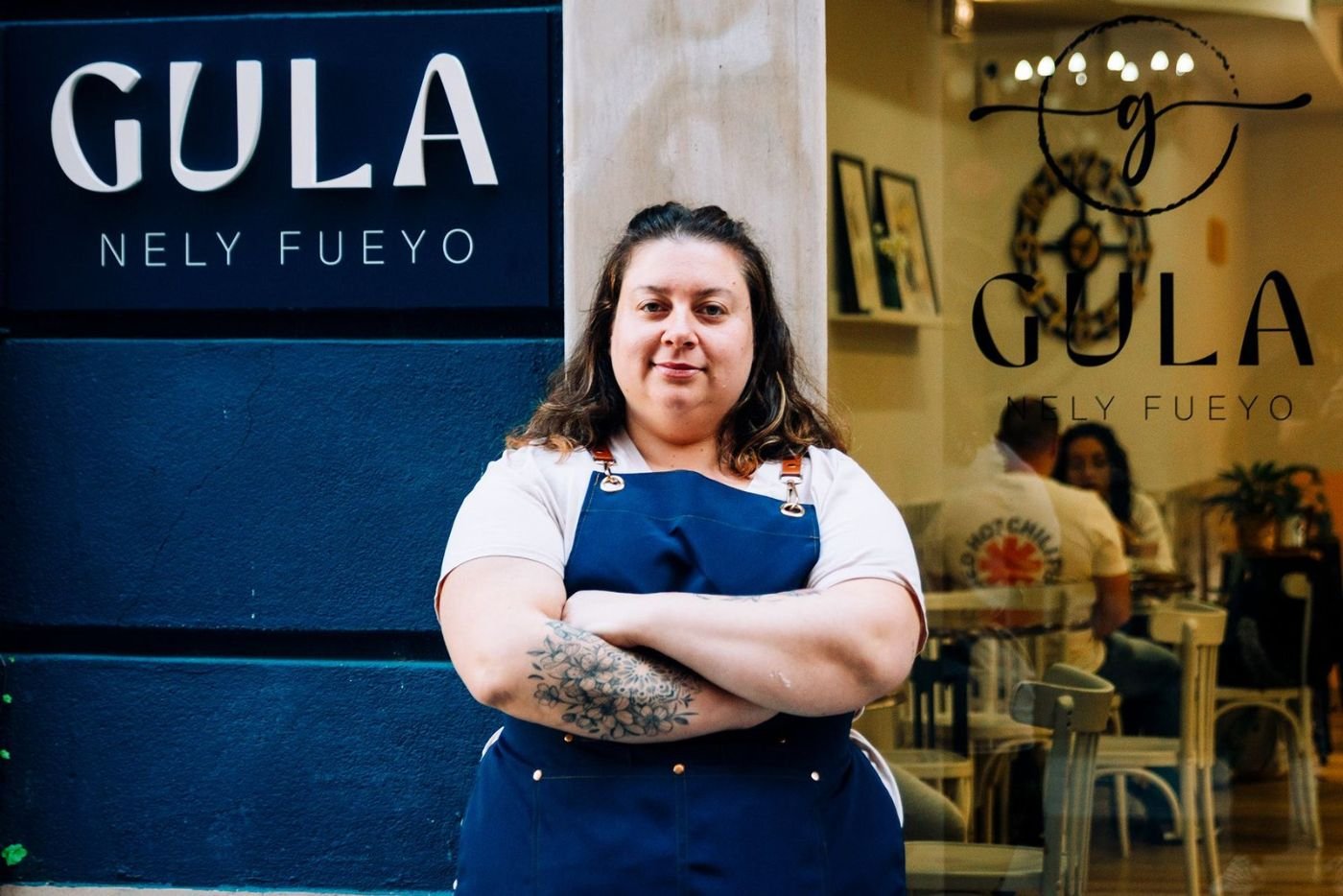 Responsable de Gula Nely posa con un plato frente al rótulo del local.