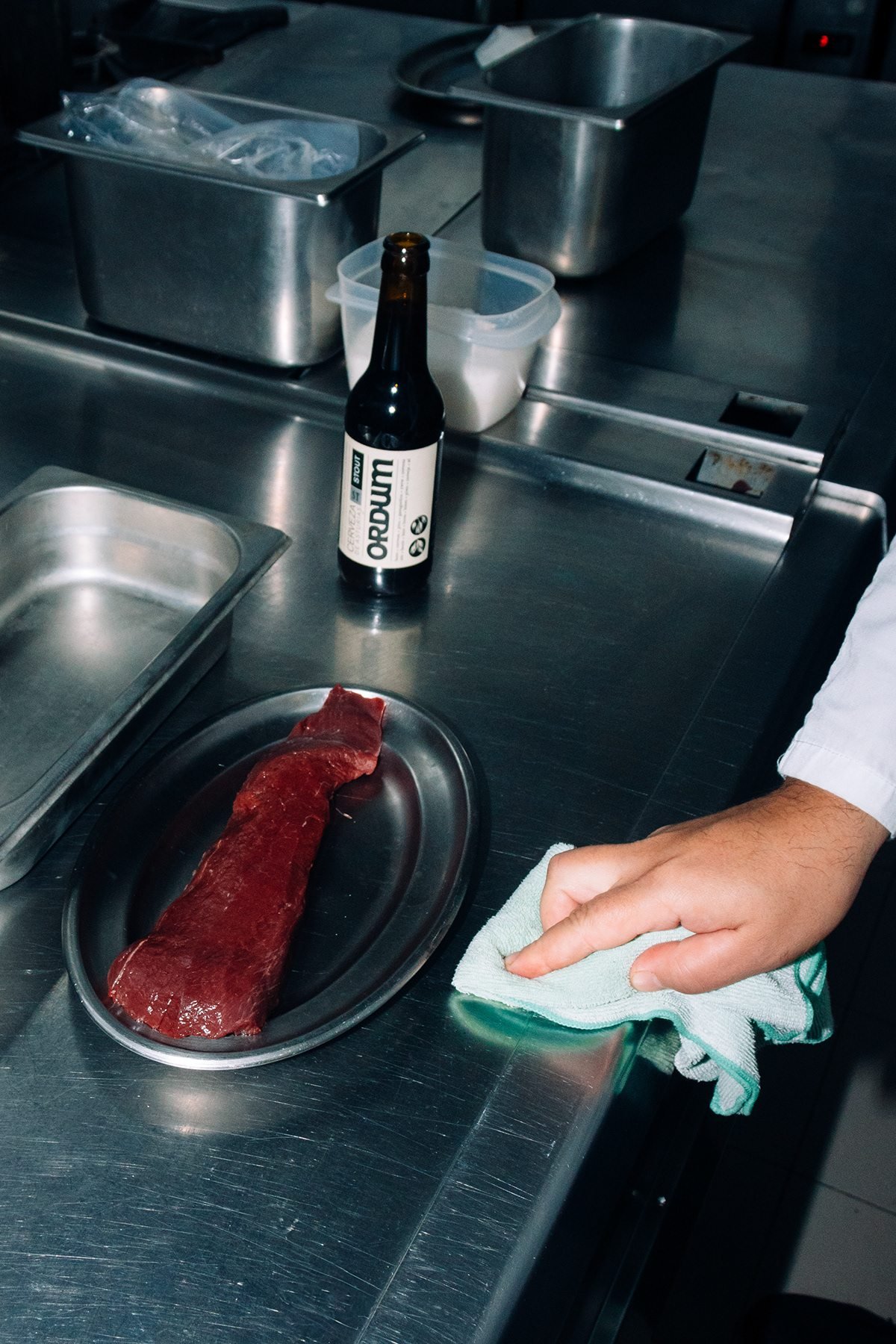 Ayalga x Ordum: pieza de carne cruda en una bandeja y botella de cerveza en la cocina