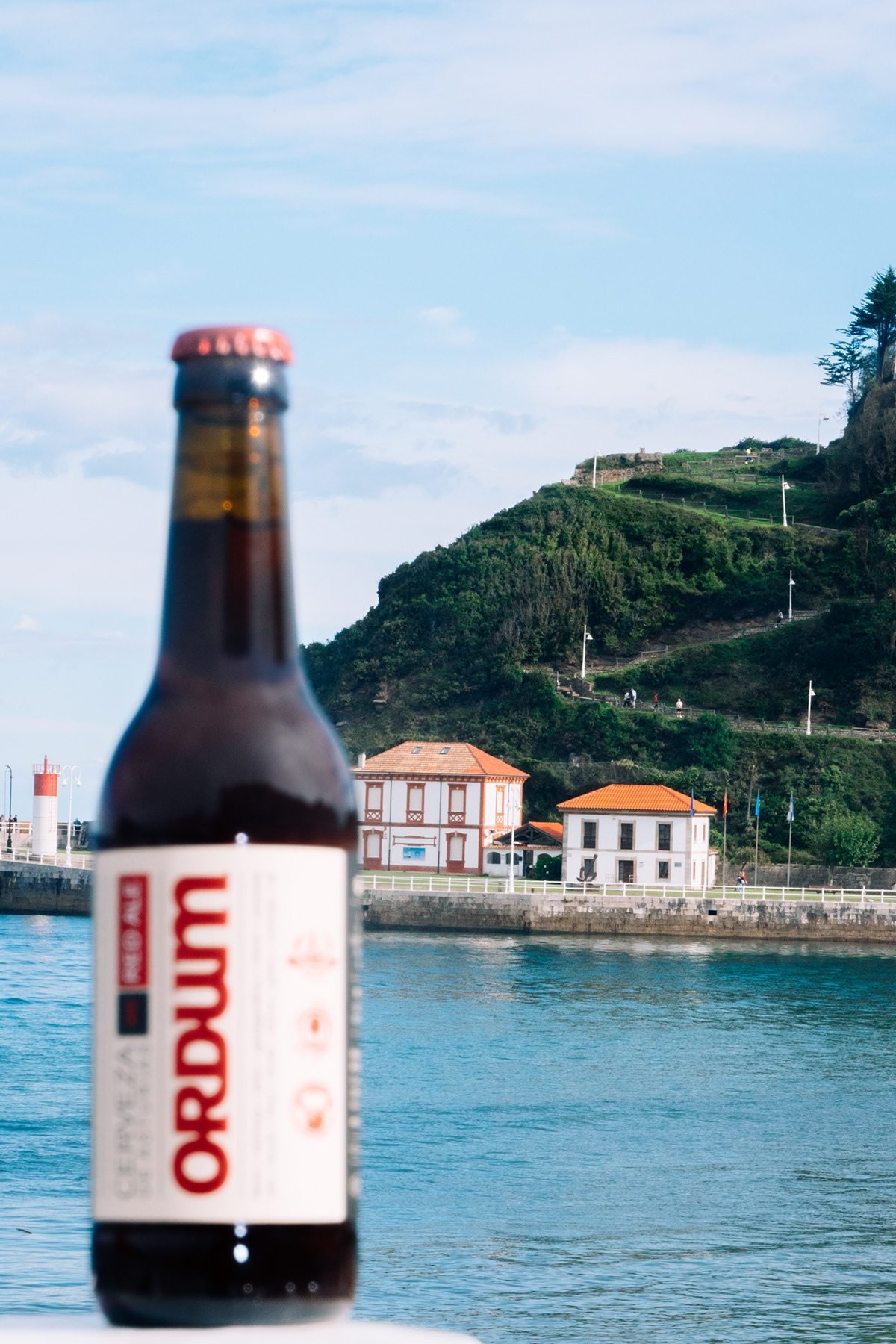 Ayalga x Ordum: botella de Ordum frente al mar y casas de la costa
