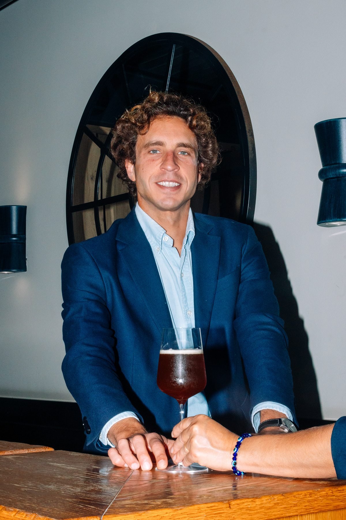 Ayalga x Ordum: hombre con americana azul sonriendo con una copa de cerveza