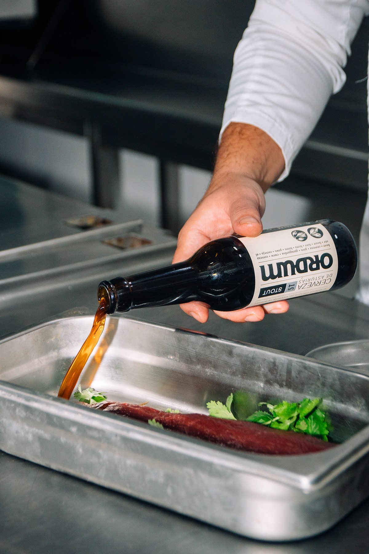 Ayalga x Ordum: mano vertiendo cerveza Ordum sobre carne en una bandeja de cocina