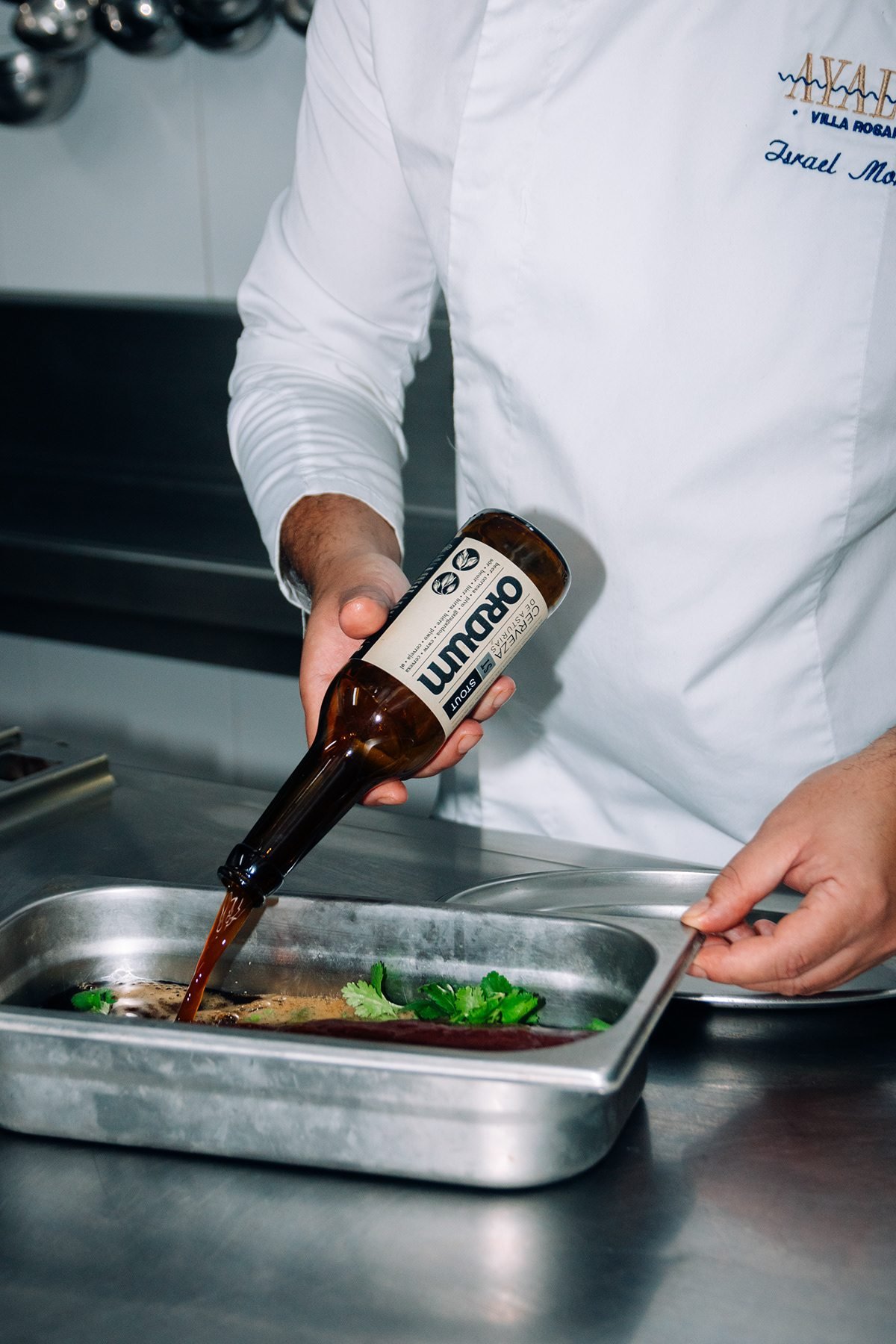 Ayalga x Ordum: cocinero vertiendo cerveza Ordum en una bandeja con carne y hojas verdes
