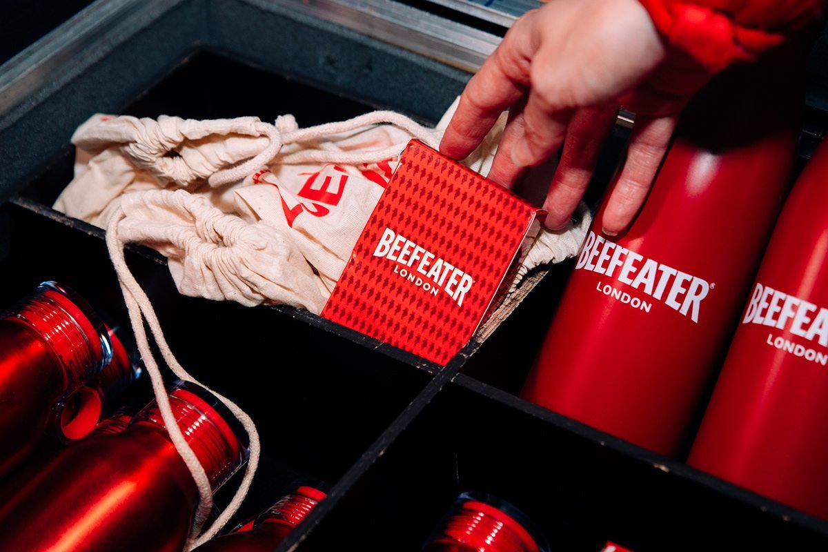 Beefeater London: mano cogiendo un folleto rojo junto a botellas térmicas y bolsas de tela