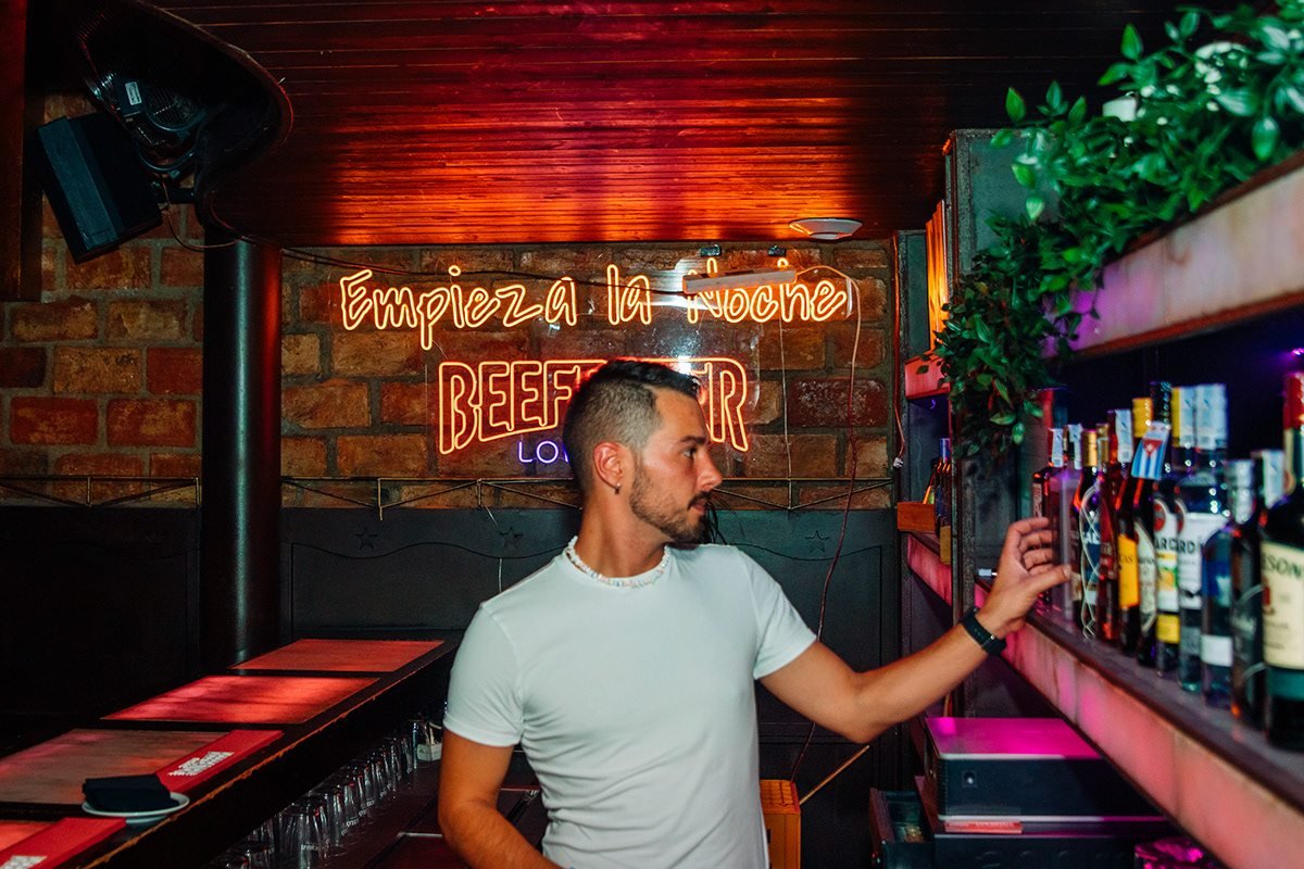 Beefeater London: hombre junto a las botellas de la barra bajo el neón «Empieza la noche»