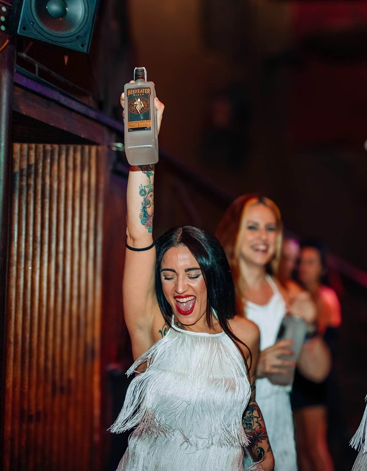 Beefeater London: mujer con vestido blanco de flecos levantando una botella en la fiesta