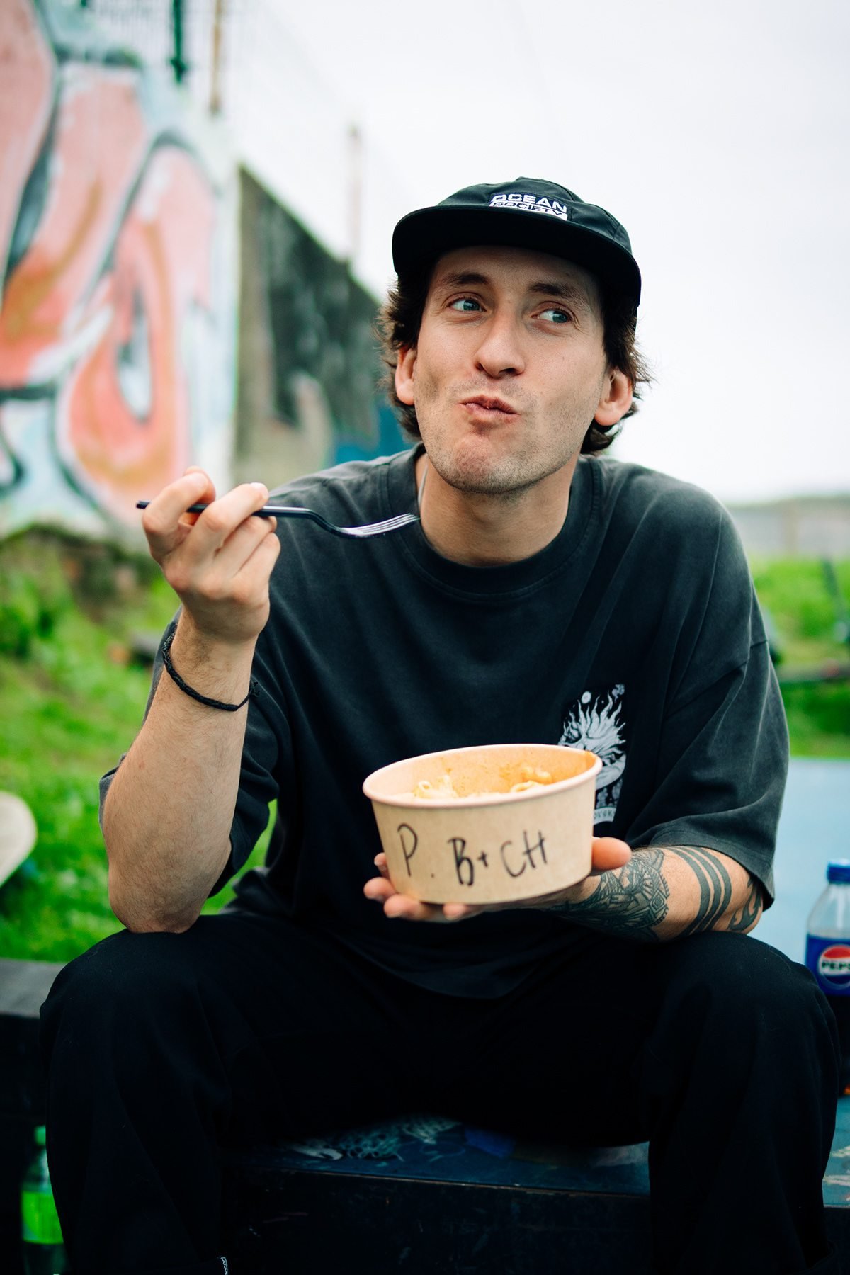 Gula: hombre con gorra comiendo de un bol de cartón ante un muro de grafitis