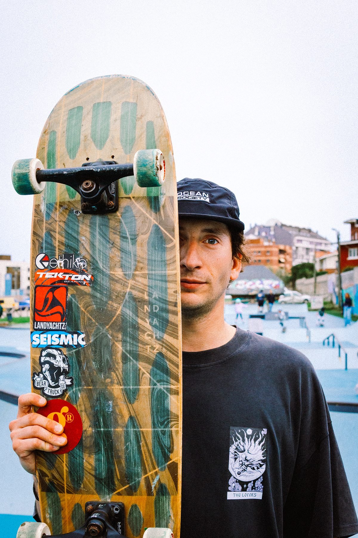 Gula: hombre con gorra sosteniendo un monopatín delante de la cara en un skatepark