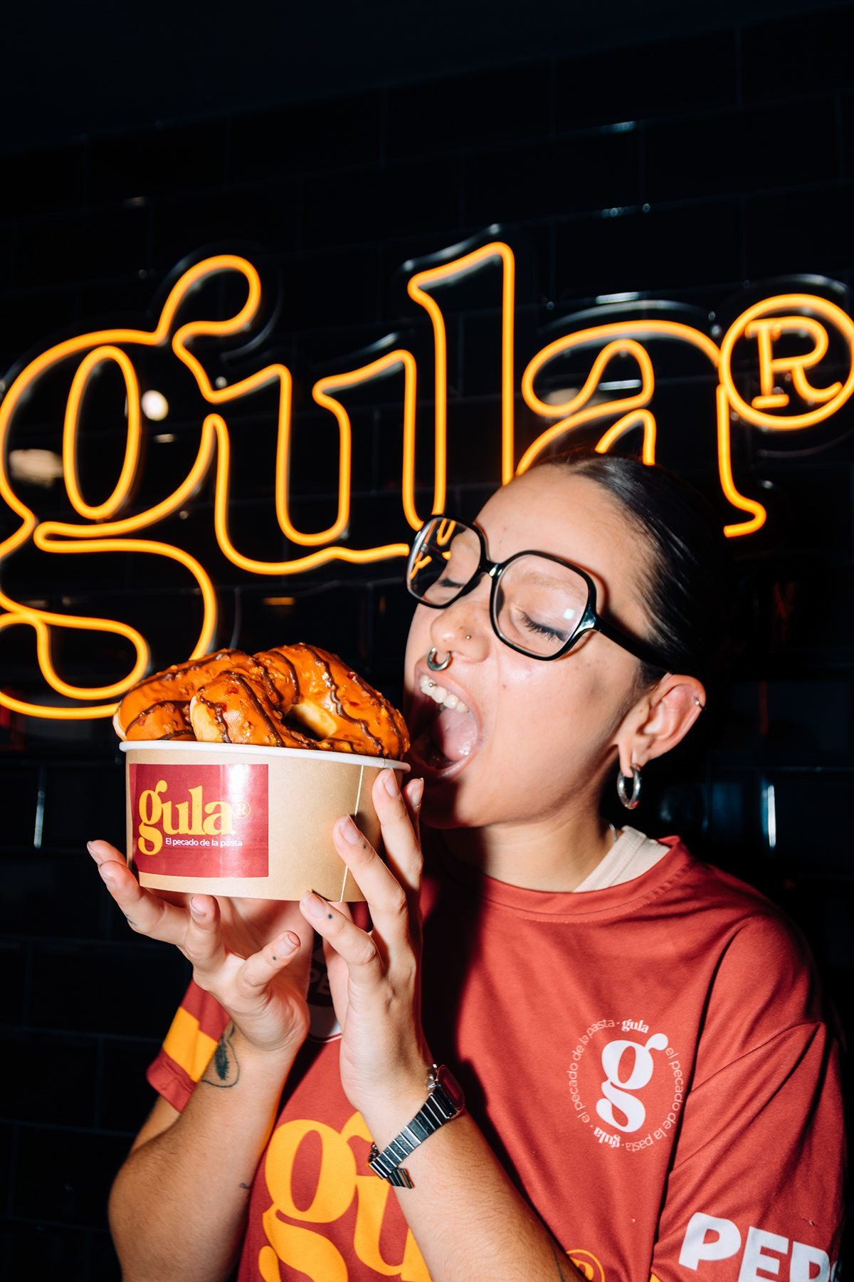 Gula: mujer con gafas mordiendo un dulce de un bol de Gula bajo el neón