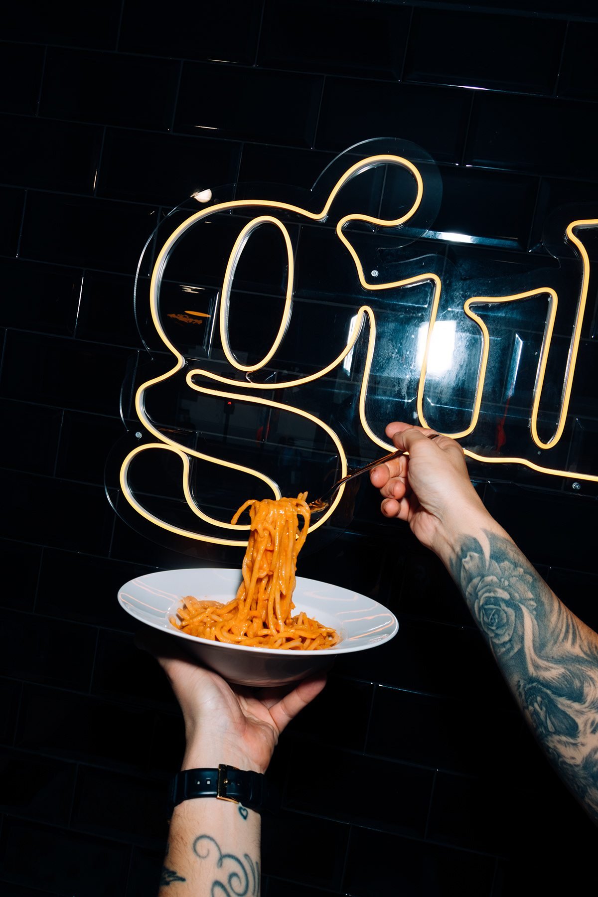 Gula: plato de pasta sostenido bajo el neón de la marca