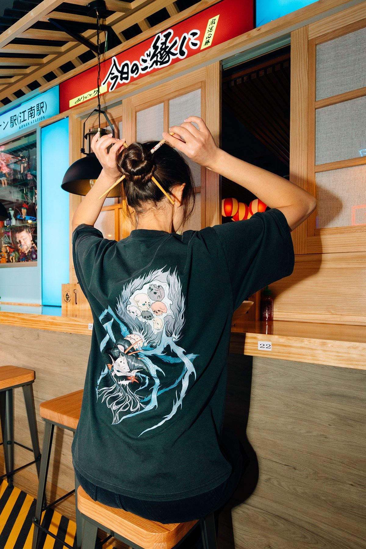 Incubu Clothing: modelo de espaldas con camiseta negra estampada en un restaurante de estilo japonés