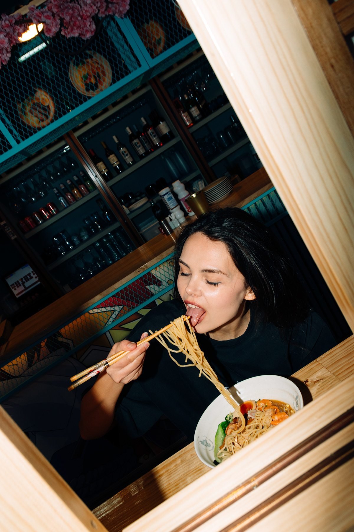 Incubu Clothing: modelo comiendo fideos con palillos tras una ventana de madera