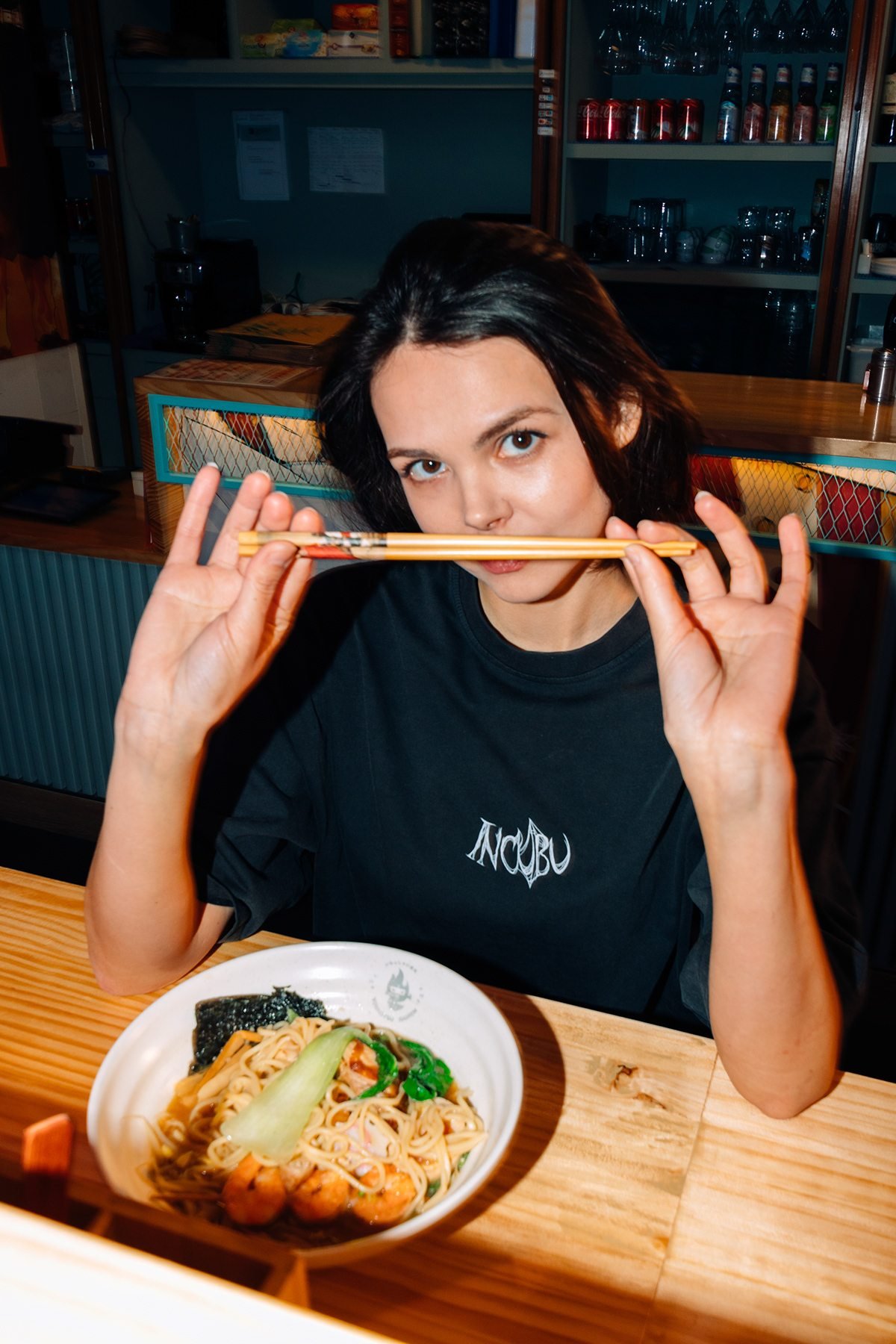 Incubu Clothing: modelo con camiseta negra sosteniendo unos palillos junto a un bol de ramen