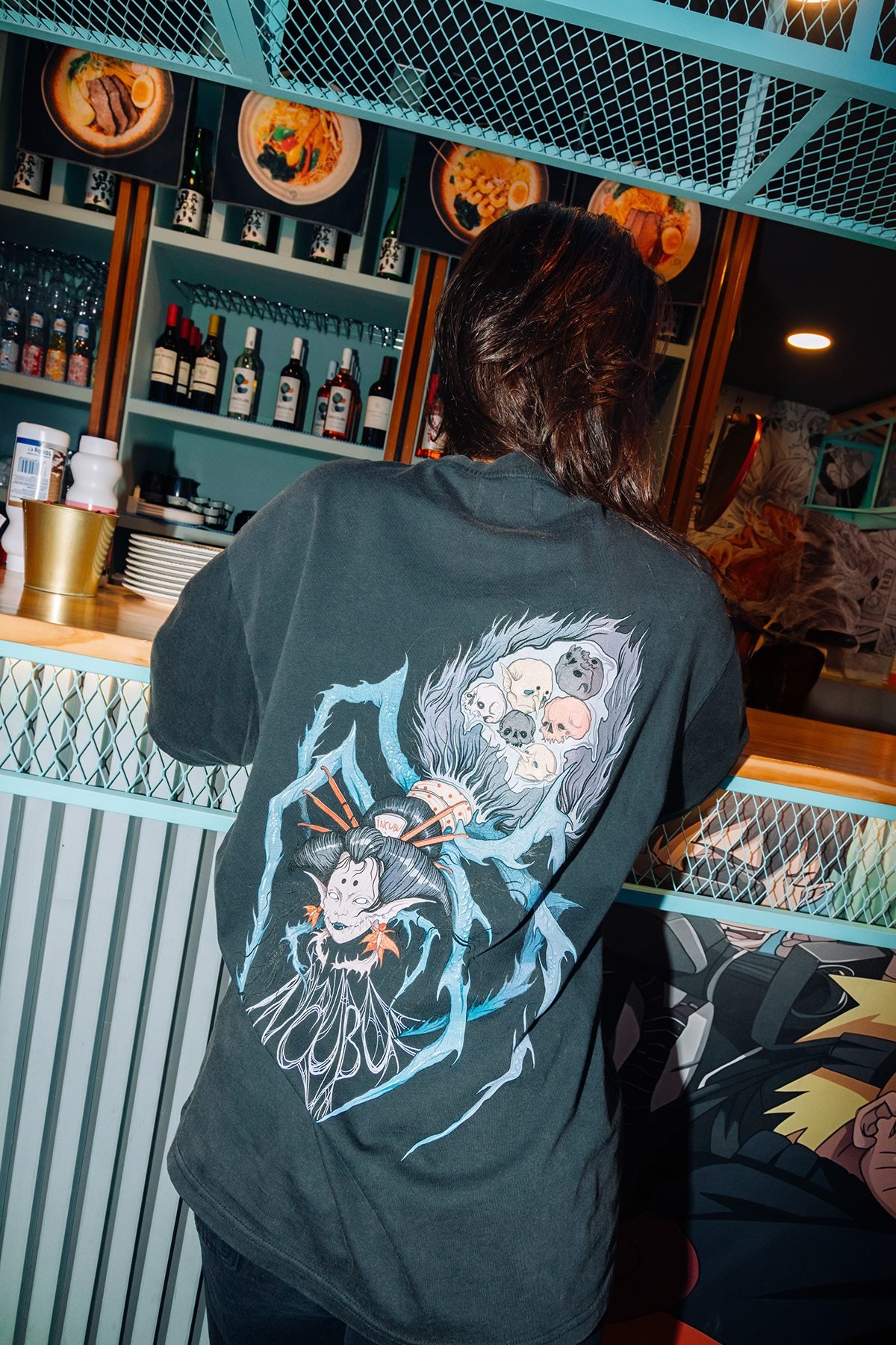 Incubu Clothing: espalda de camiseta negra con ilustración estampada en un restaurante