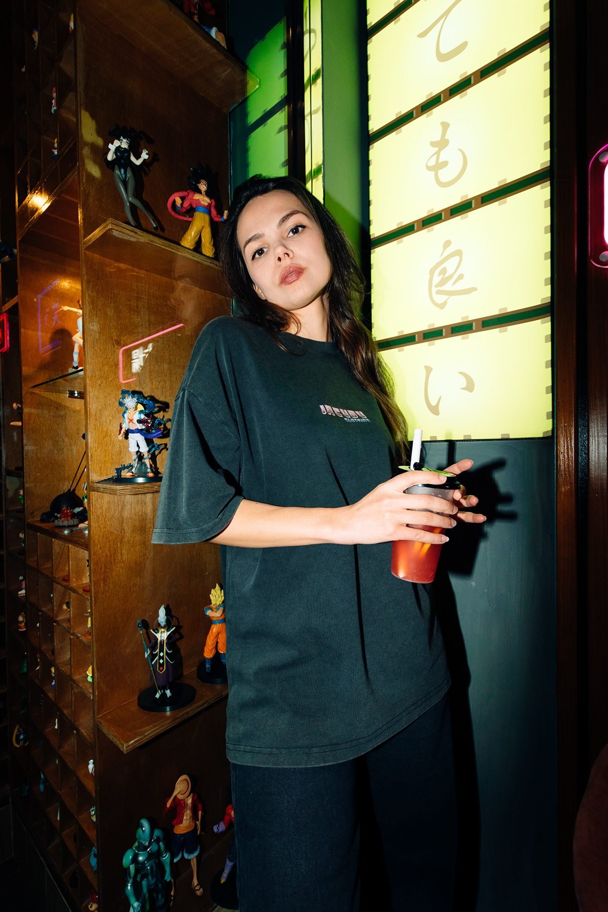 Incubu Clothing: modelo con camiseta negra y una bebida junto a un rótulo luminoso amarillo