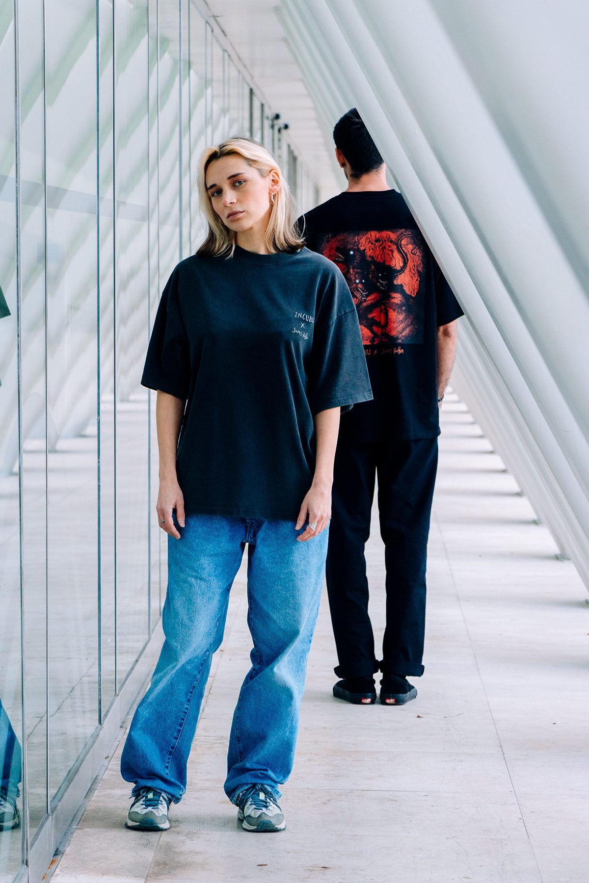 Incubu Clothing: modelo con camiseta negra y vaqueros en un pasillo de arcos blancos