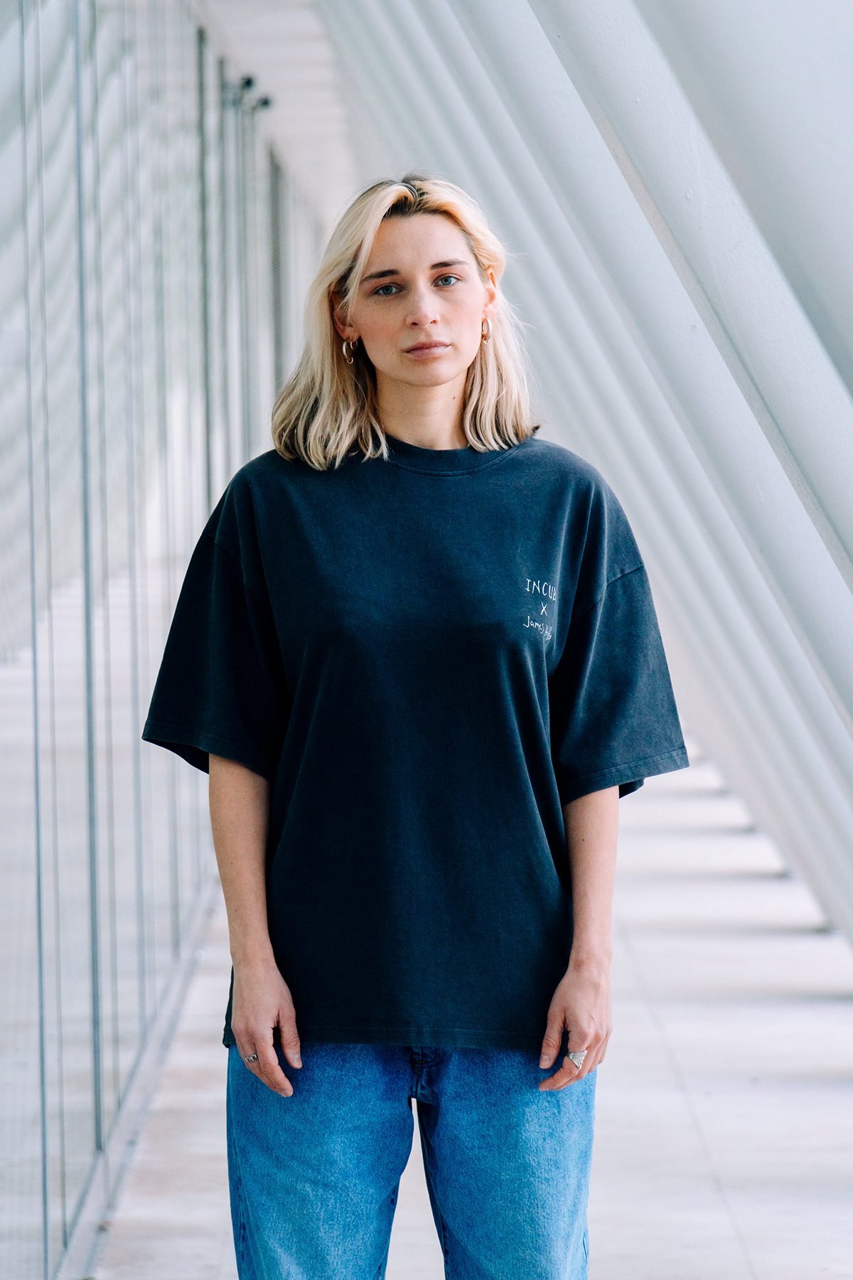 Incubu Clothing: retrato de modelo con camiseta negra en un pasillo de arcos blancos