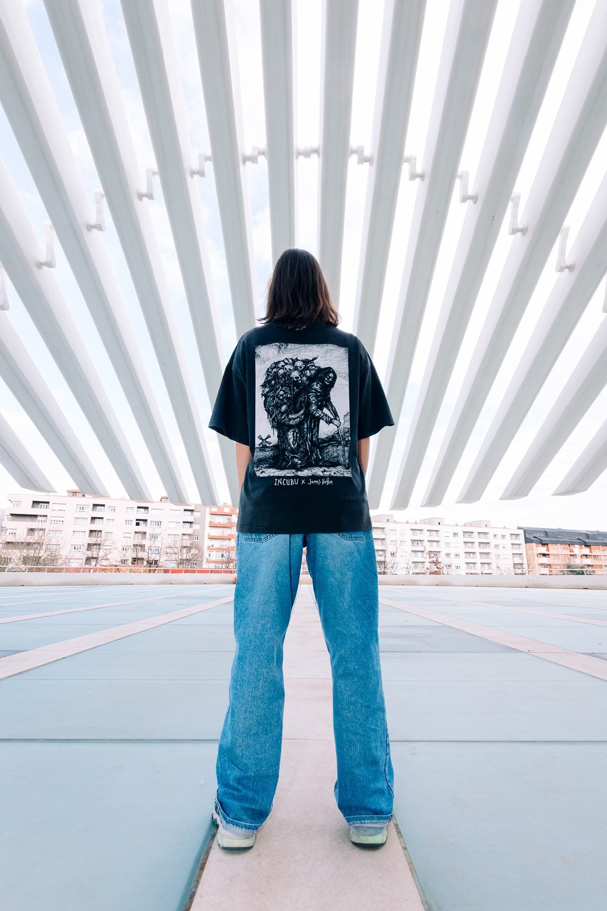 Incubu Clothing: modelo de espaldas con camiseta estampada bajo una estructura de arcos blancos
