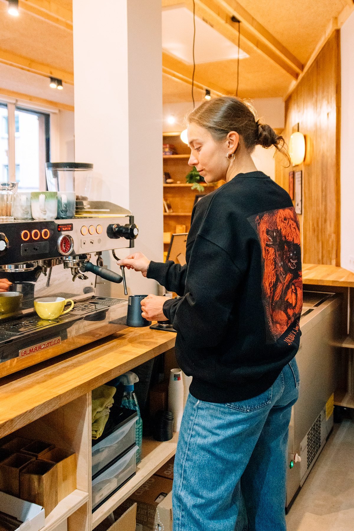 Incubu Clothing: modelo con sudadera negra estampada junto a una cafetera