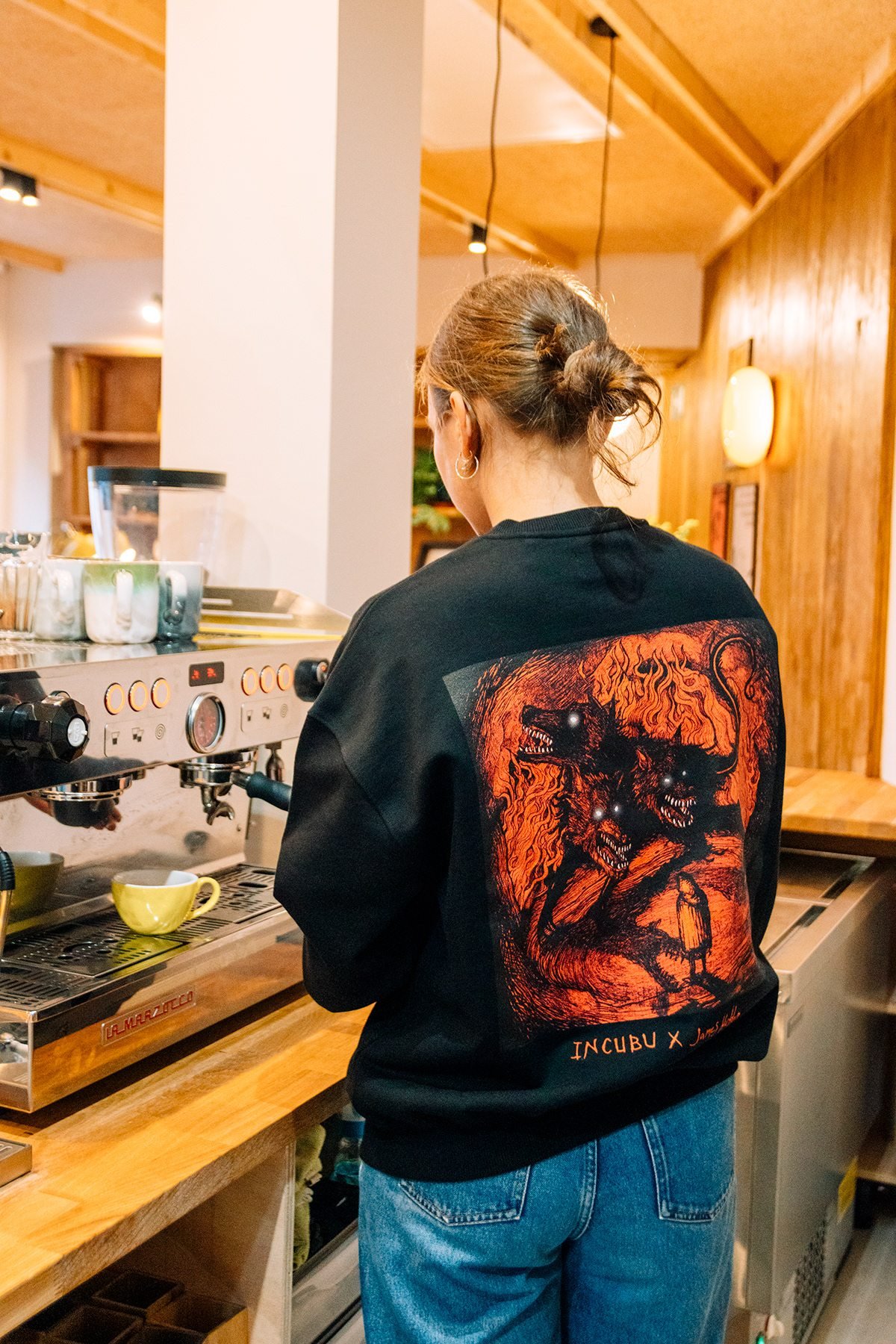 Incubu Clothing: espalda de sudadera negra con estampado rojo en una cafetería
