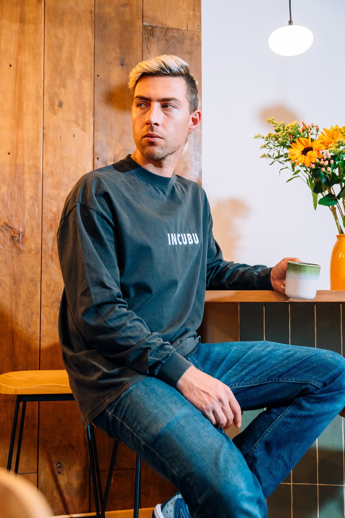 Incubu Clothing: modelo con sudadera gris sentado en un taburete junto a un mostrador