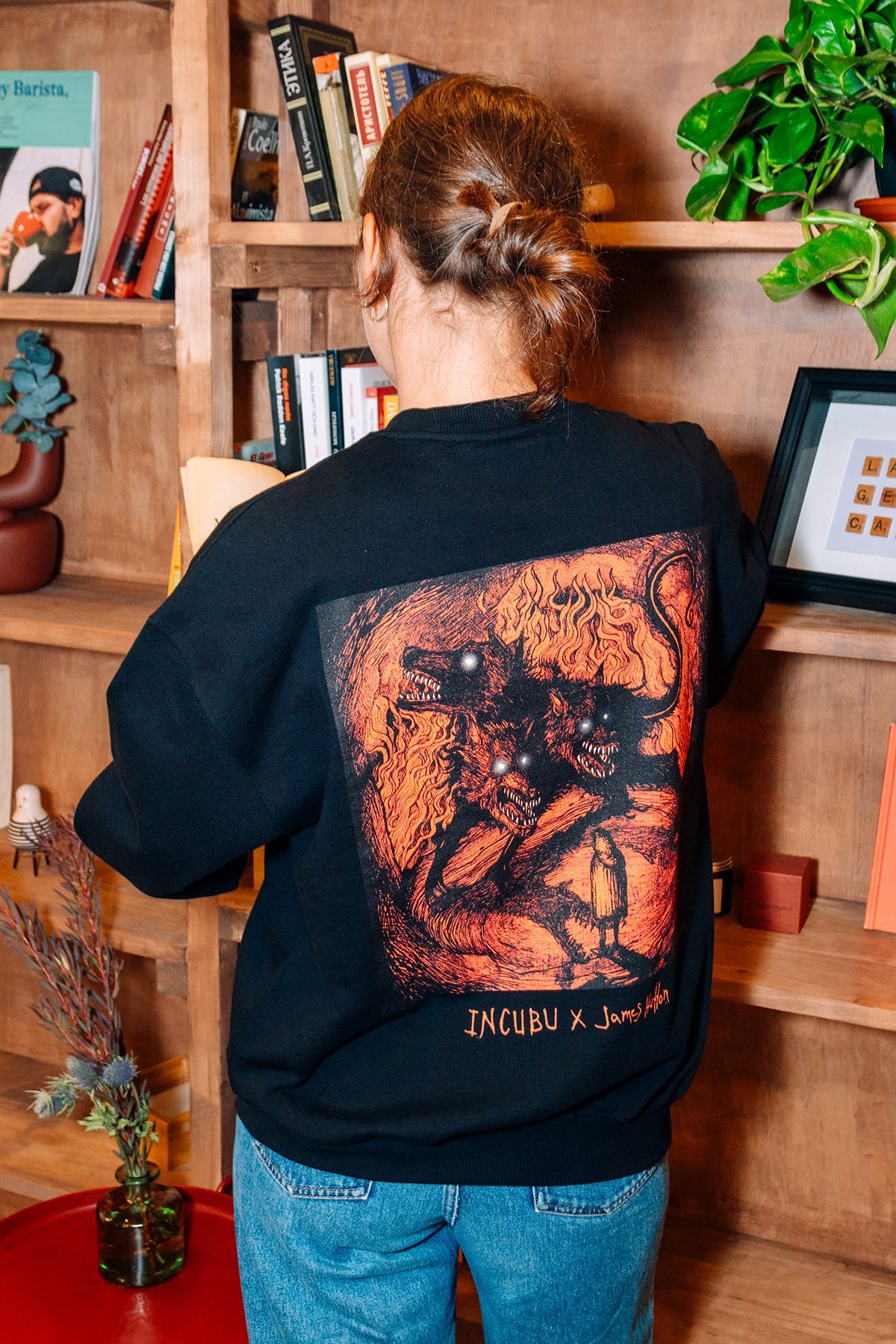 Incubu Clothing: espalda de sudadera negra con ilustración estampada junto a una estantería