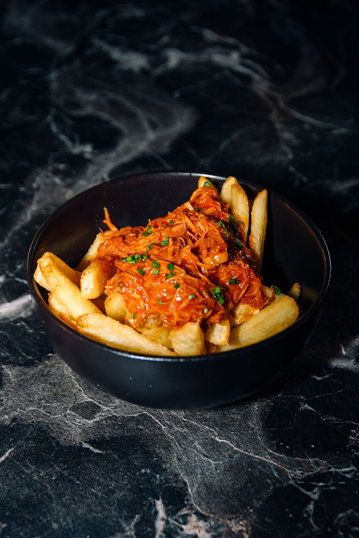 Mr Kong: bol de patatas fritas con carne desmechada sobre mesa de mármol negro