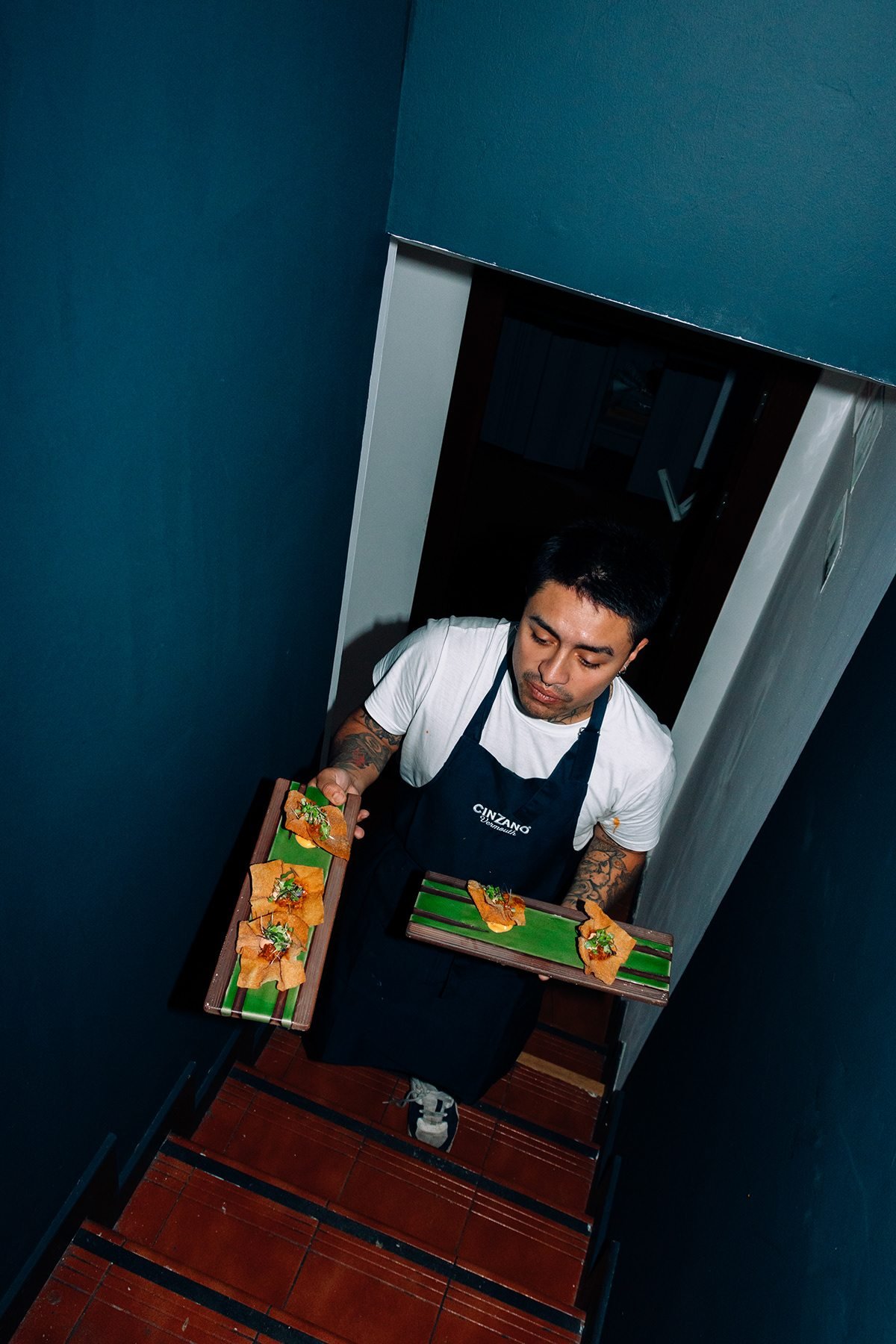 Mr Kong: camarero subiendo una escalera con dos tablas de comida, visto desde arriba