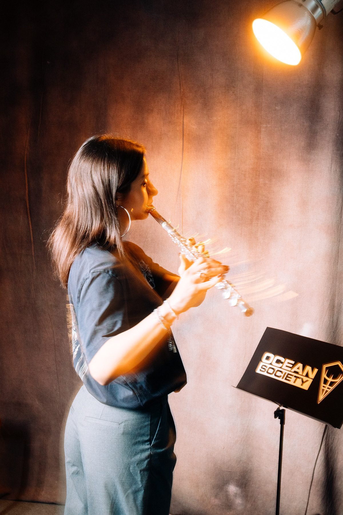 Ocean Society: mujer tocando un instrumento de viento junto a un atril con el logotipo de la marca