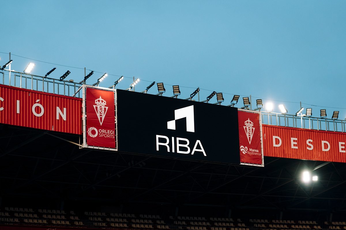 Riba Spaces: logotipo de RIBA en la grada del estadio junto a escudos rojiblancos