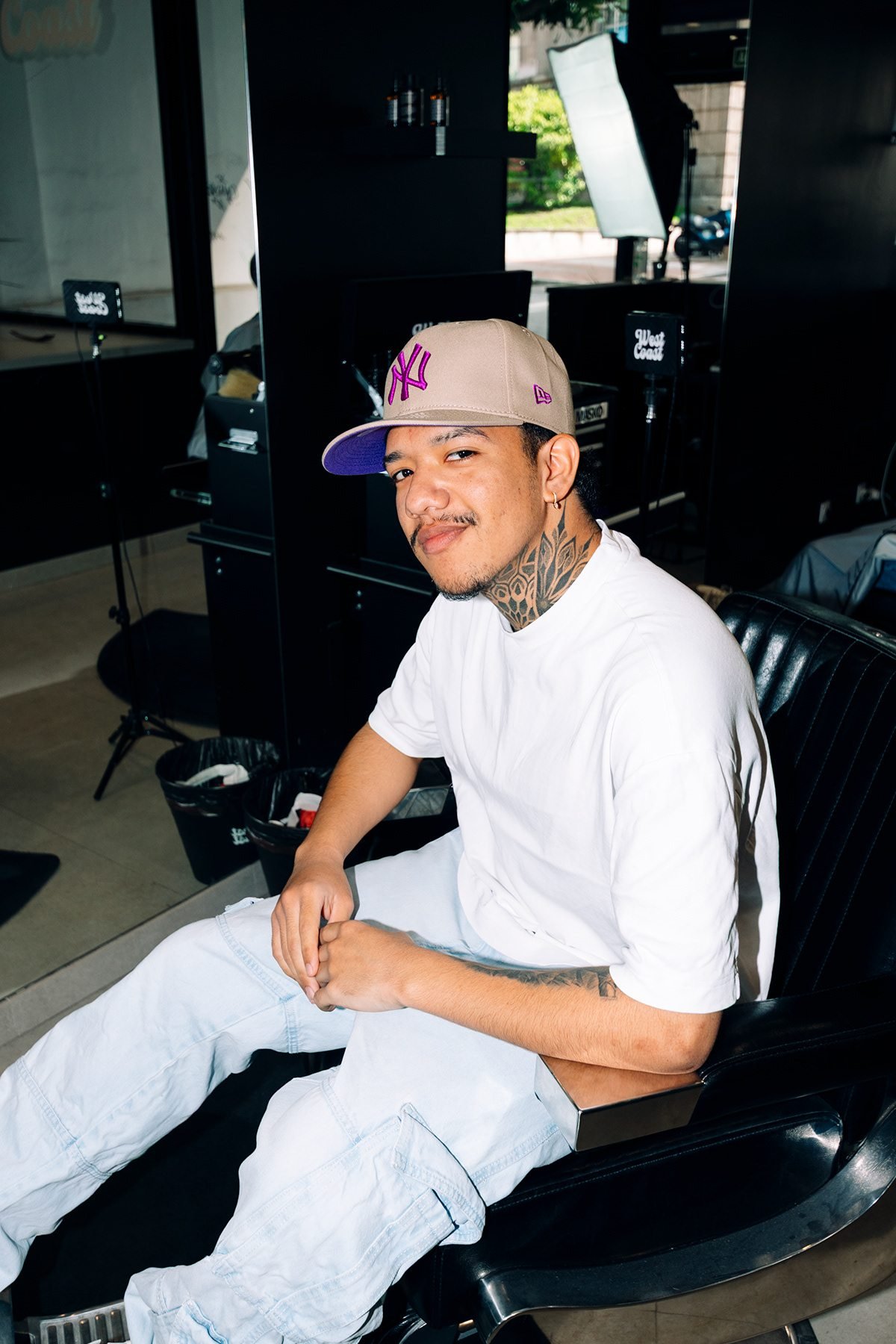West Coast: cliente con gorra sonriendo en el sillón de la barbería