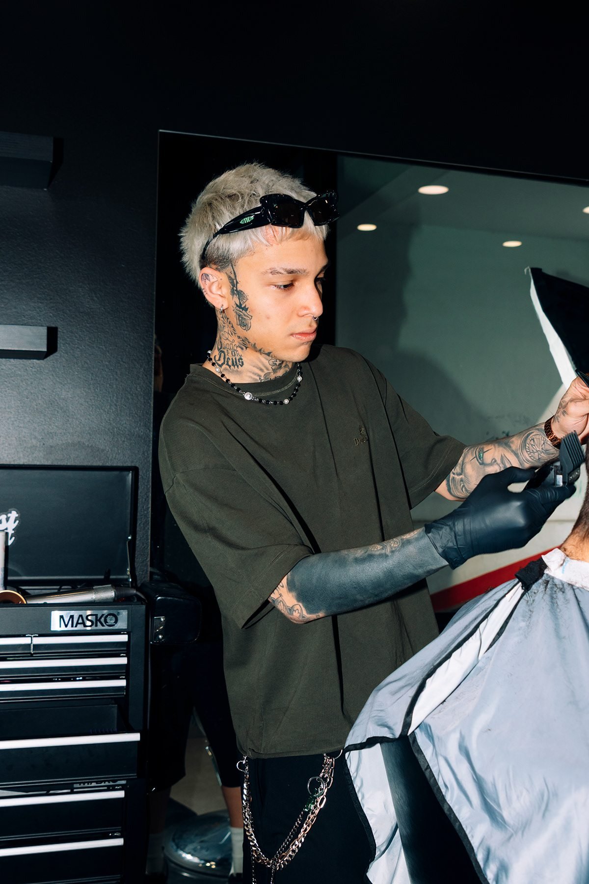 West Coast: barbero con guantes negros cortando el pelo a un cliente