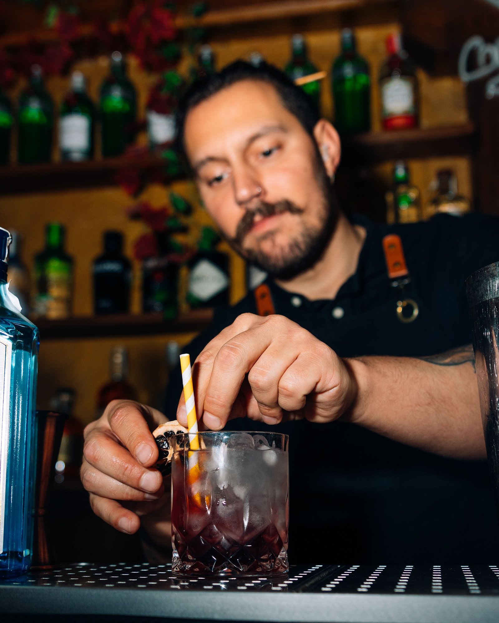 Barista agita una coctelera delante de una estantería de botellas.