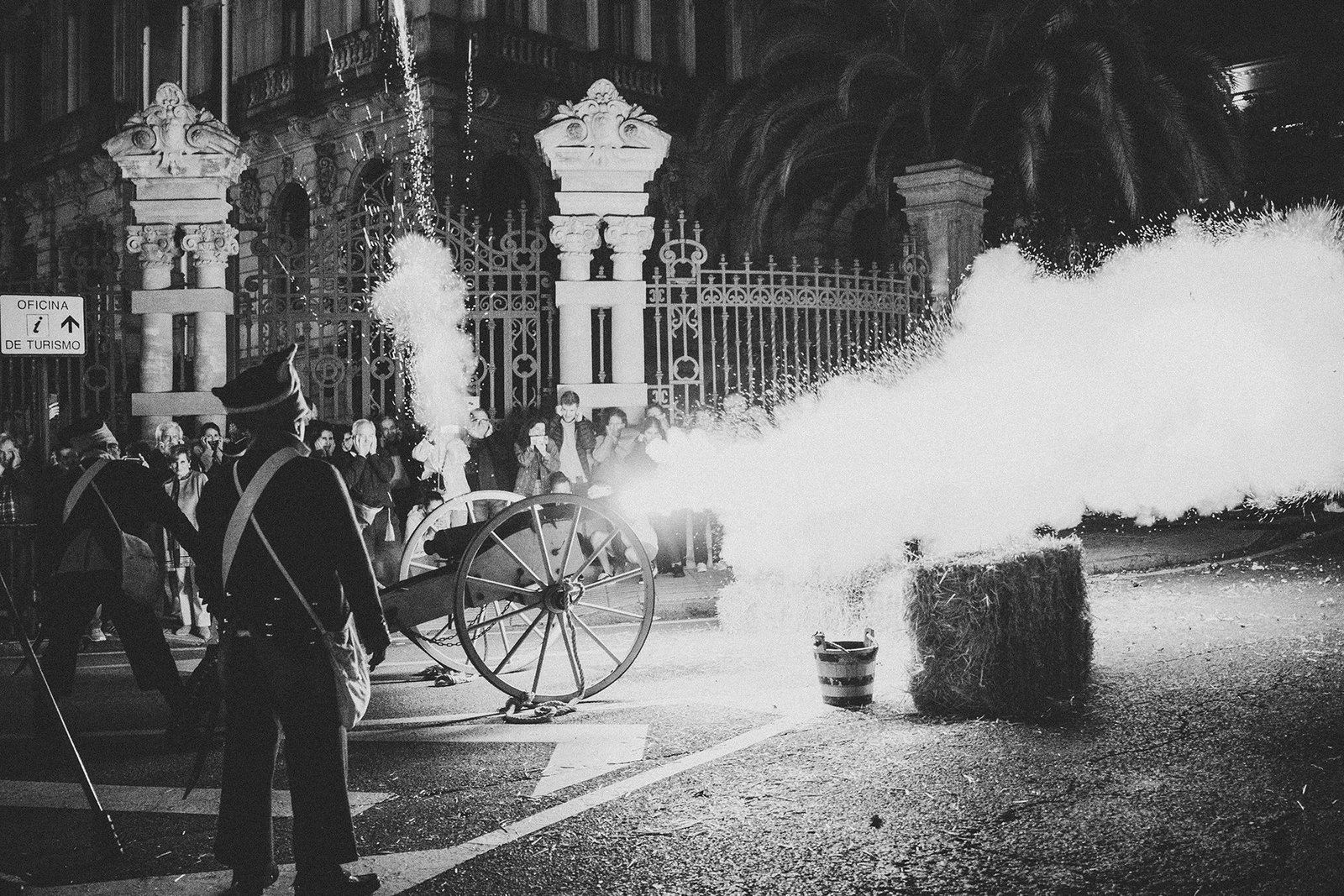 Procesión nocturna entre edificios históricos y humo escénico.