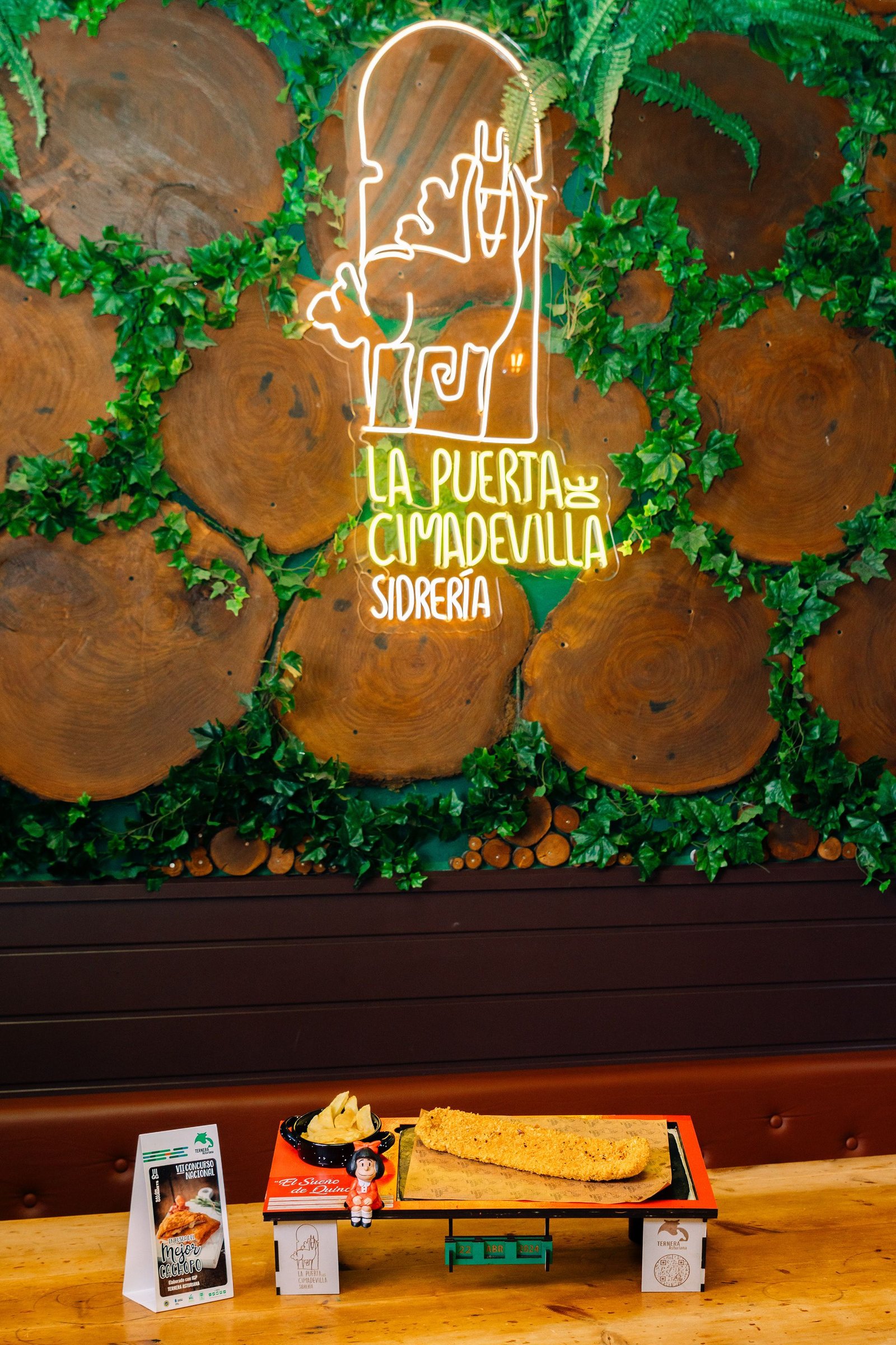 Comedor de sidrería con mural iluminado y mesas preparadas.