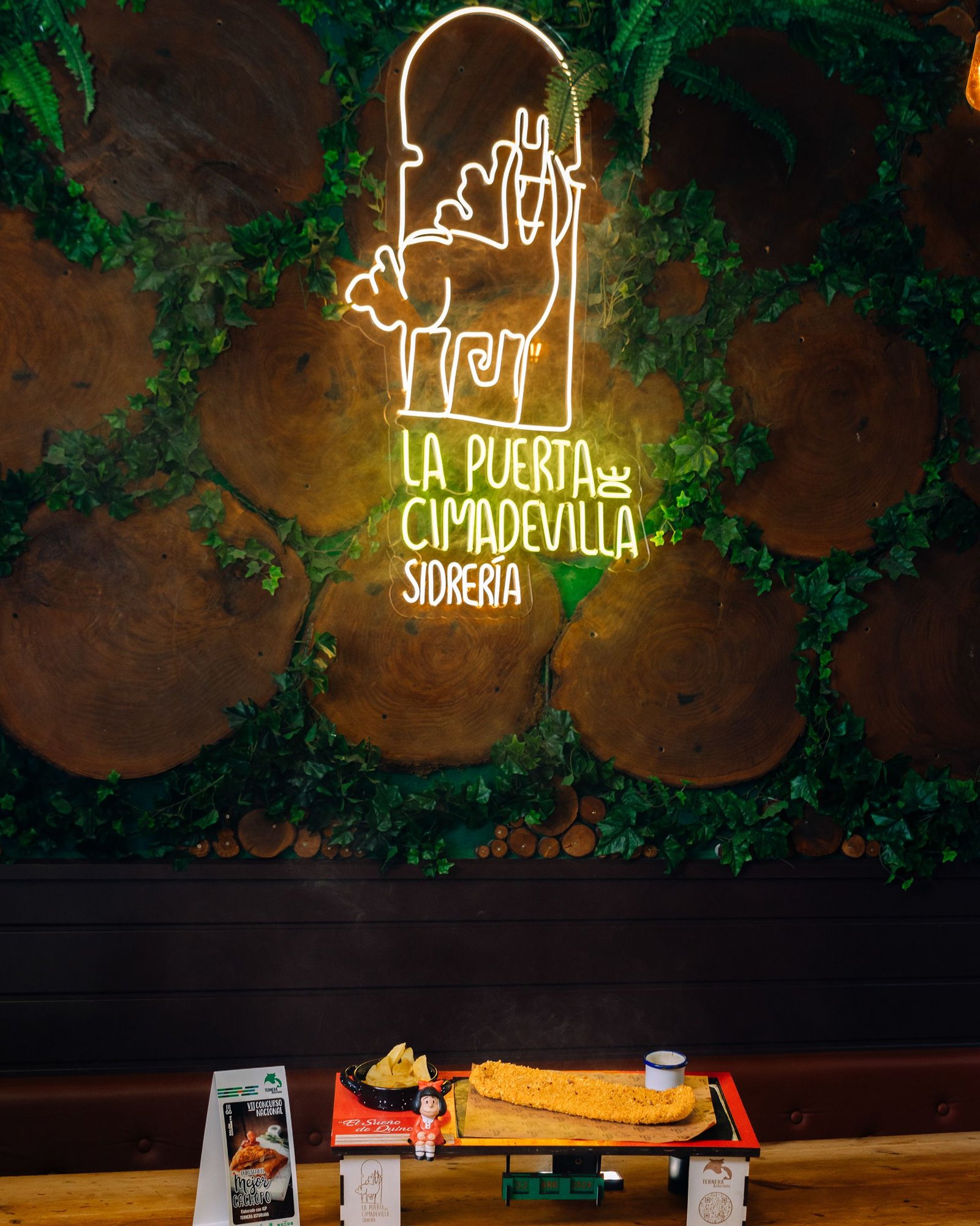 Pared decorativa de La Puerta de Cimadevilla iluminada en el comedor.