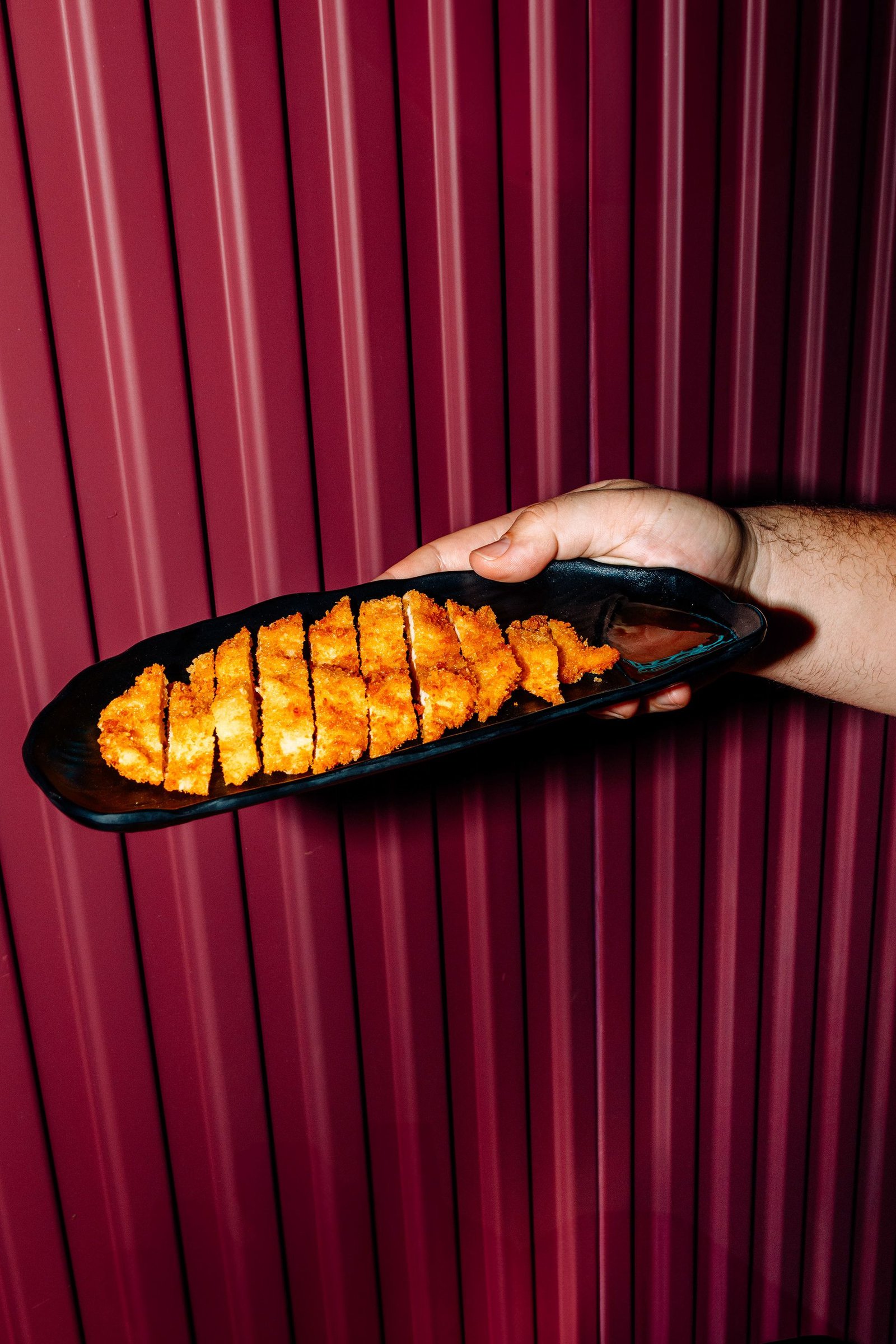 Pieza de sushi sostenida con palillos sobre fondo rojo.