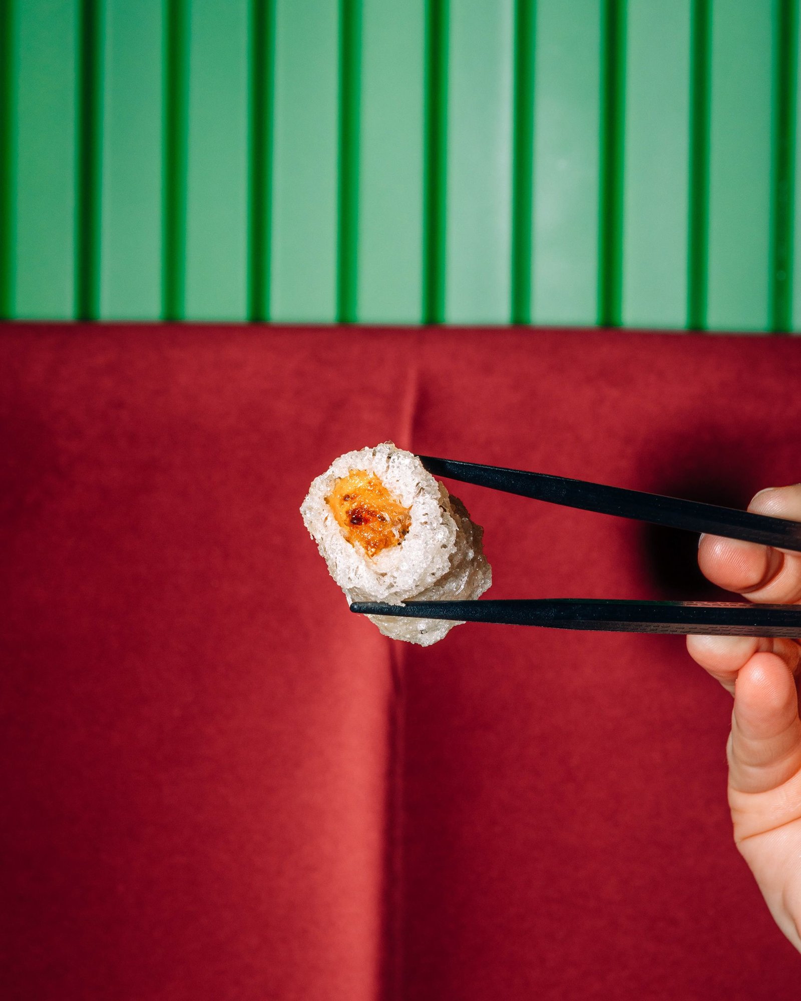 Palillos levantan una pieza de sushi sobre un plato.