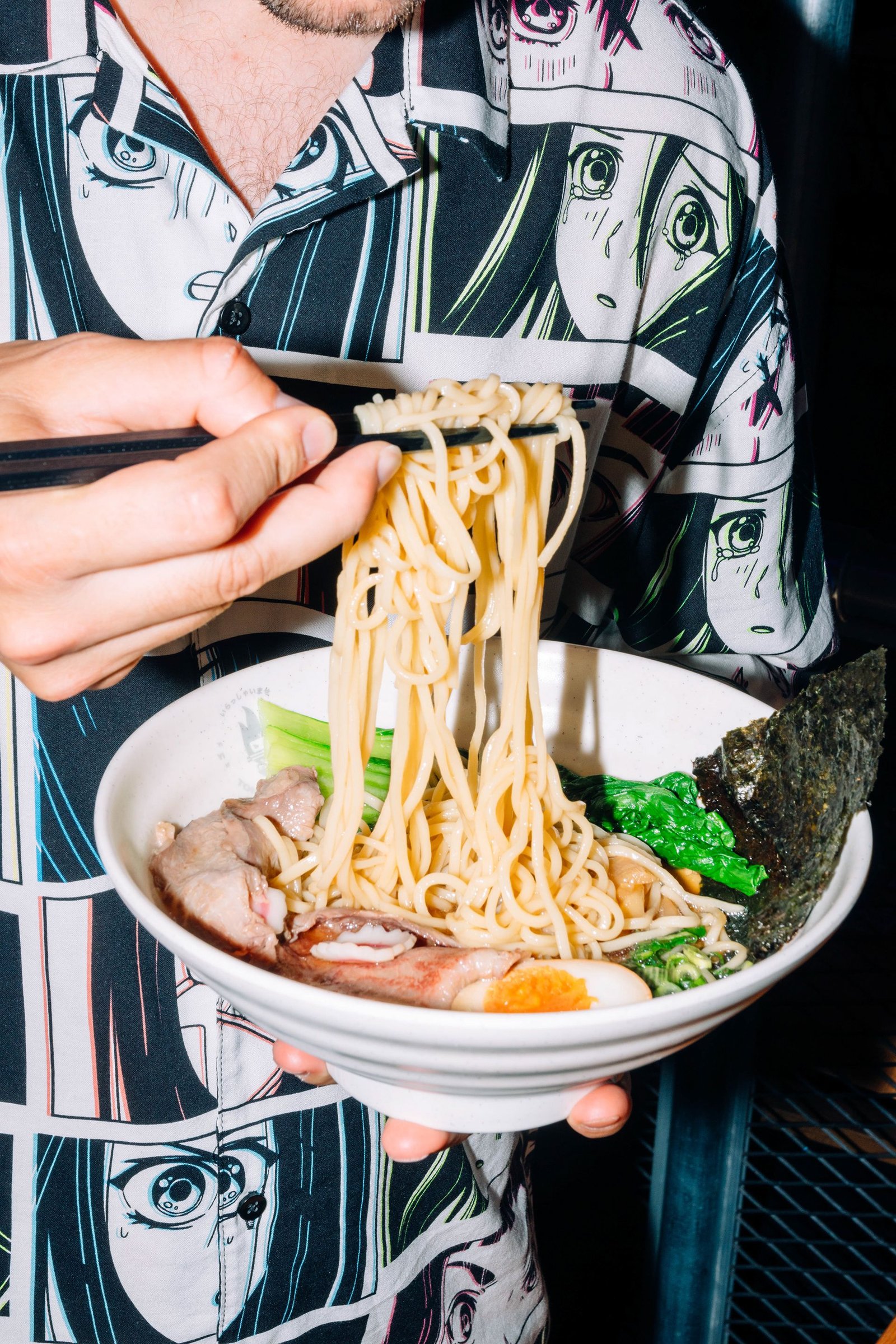Comensal acerca fideos a un bowl con los palillos.
