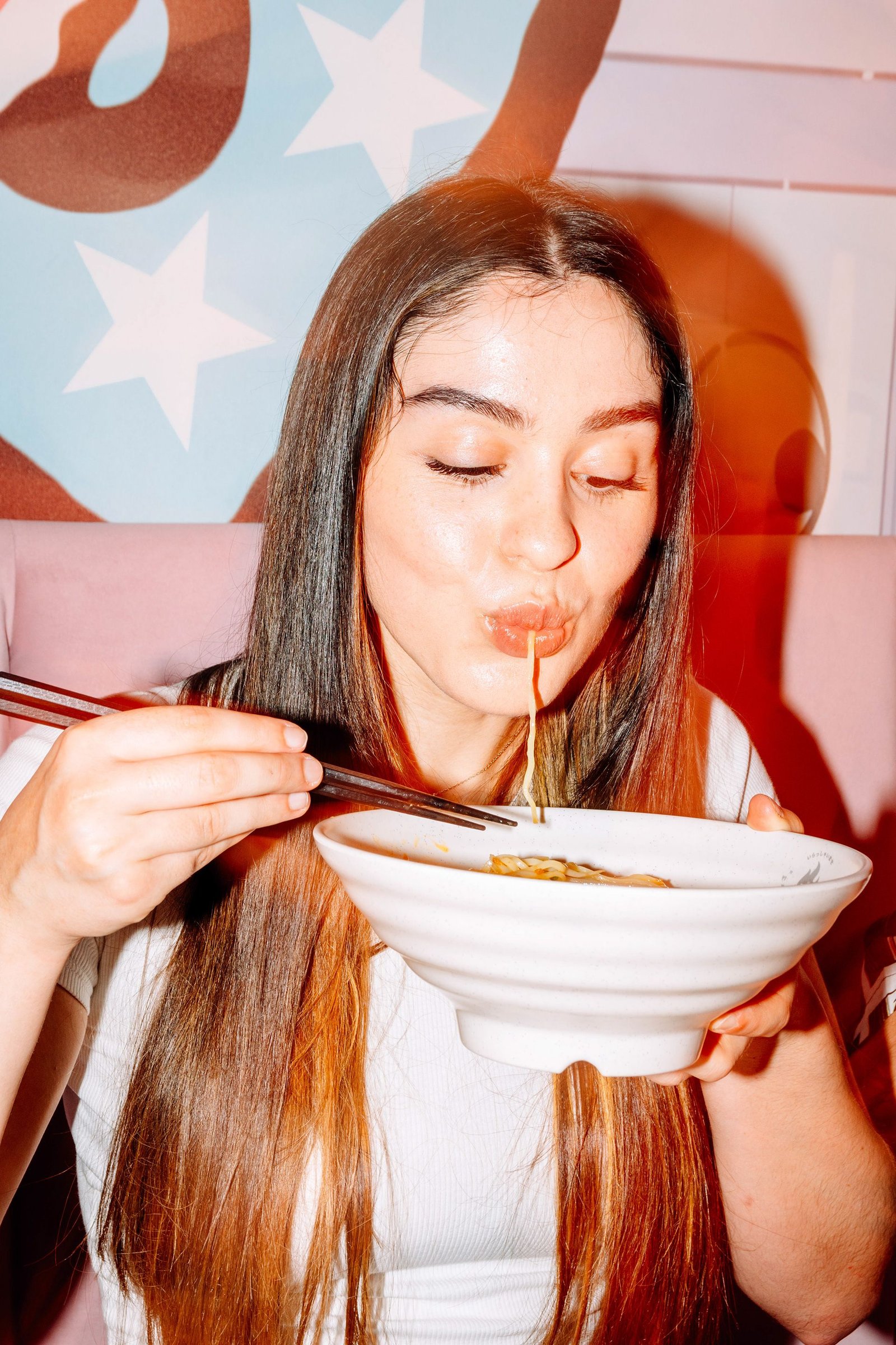 Mujer come ramen con palillos en una mesa.