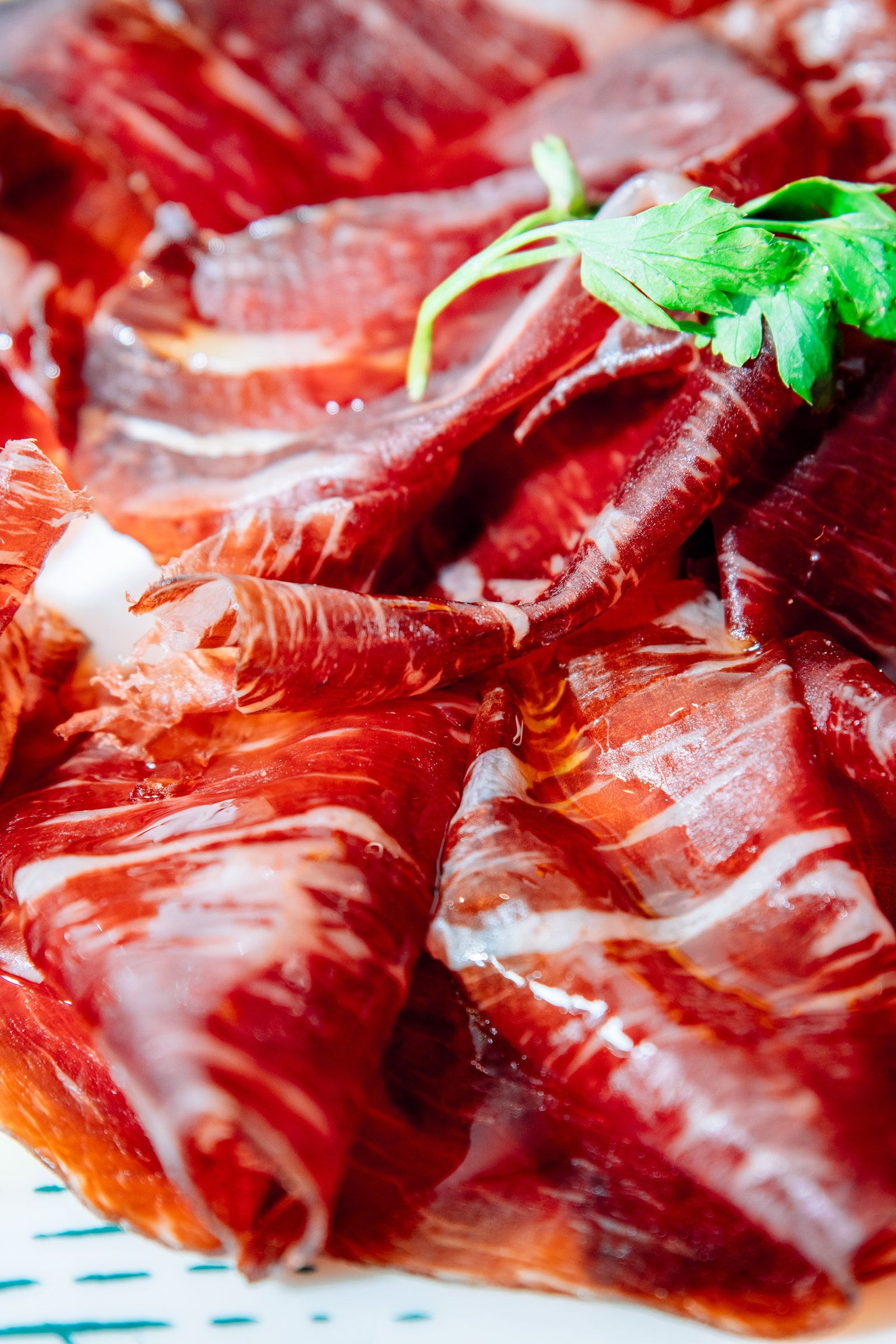 Lonchas de jamón curado con una hoja de perejil, en primer plano.