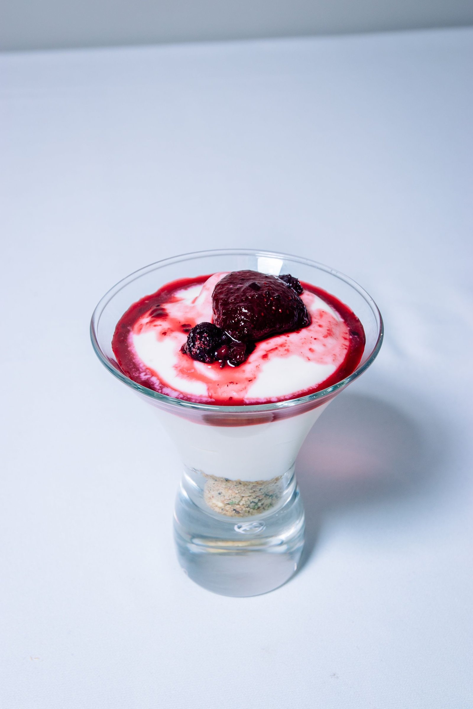 Vasito de postre con crema y frutos rojos.