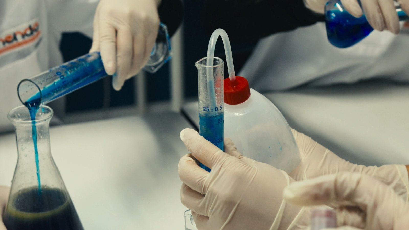 Manos con guantes pasan líquido azul de un tubo a un matraz.